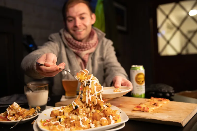 A man gets a forkfull of loaded tater tots.