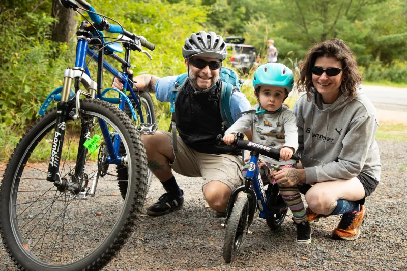 A man and woman crouch for a photo with their small child on a mountain bike.