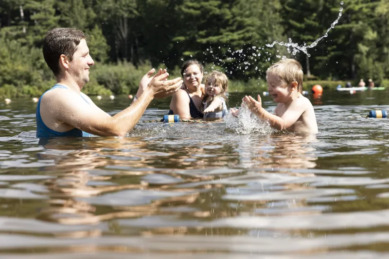 A family of adults and small children splash in the calm water of a lake.