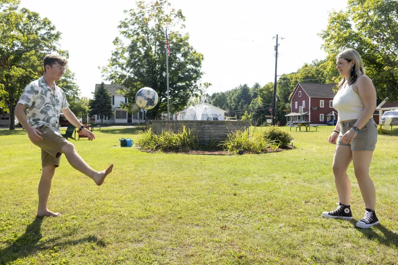 A couple people kick a soccer ball at a village green