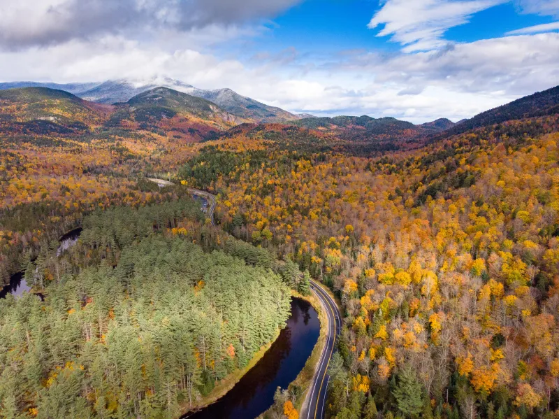 An aerial view of a single road weaving along a river in a mountain valley.