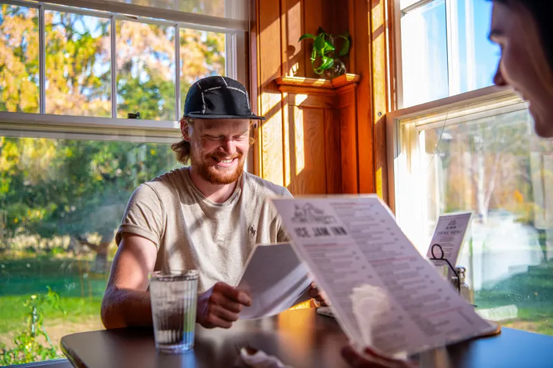 A couple looks at a menu at the Ice Jam Inn sitting next to windows on a bright day.