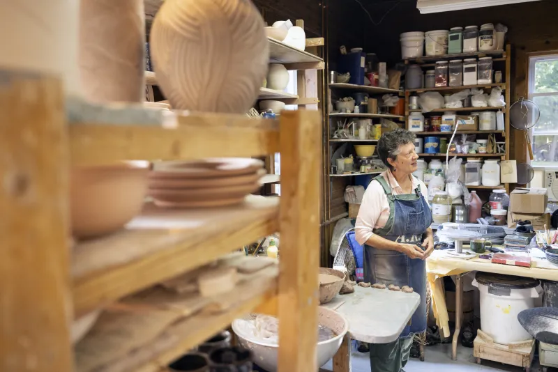 Woman standing in front of pottery projects and art supplies at Jay Craft Center.