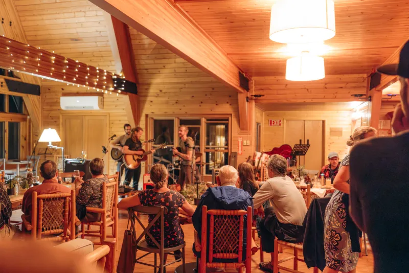 A crowd dances and listens to music in a warm-lit lodge.