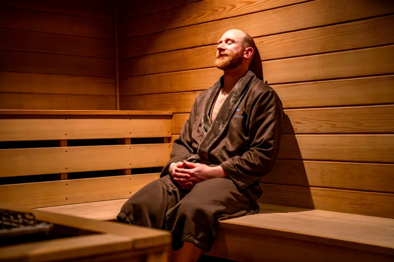 A man relaxes in a sauna with a brown robe on.