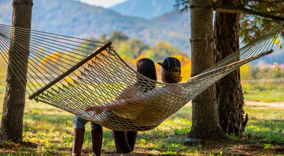 A man and woman sit in a hammock looking at fall foliage mountain views