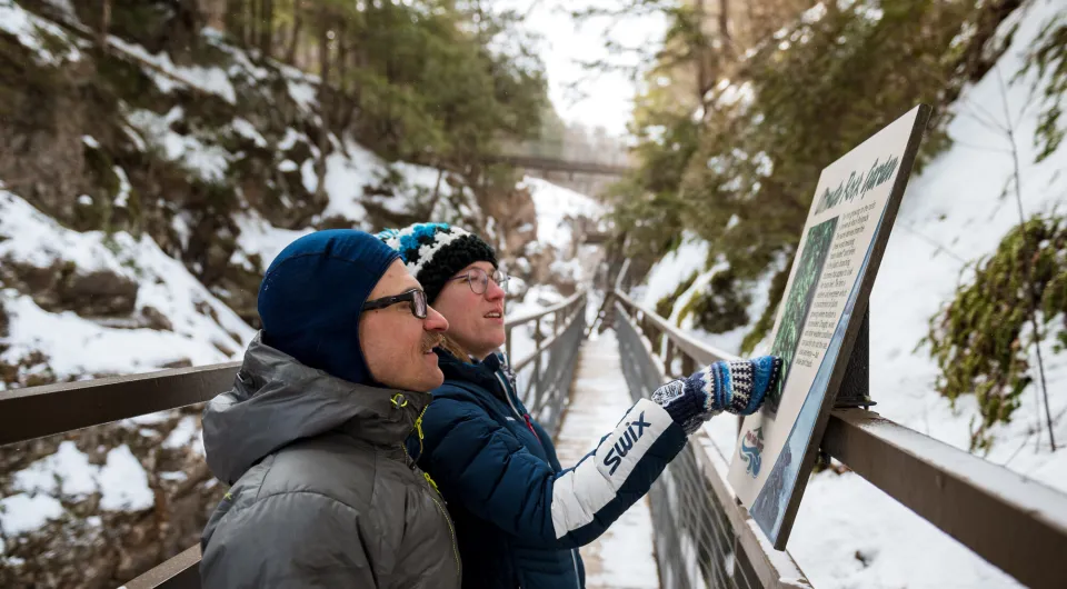 Two people bundled up on a winter hike along a boardwalk in a canyon.