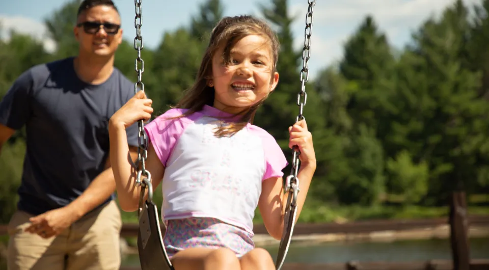 a man pushes a young girl on a swing.