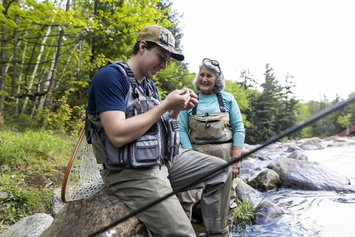 A woman helps another angler tie a fly on.