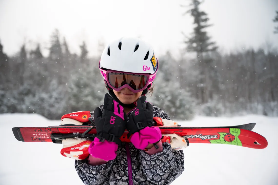 A young girl smiles while holding her skis