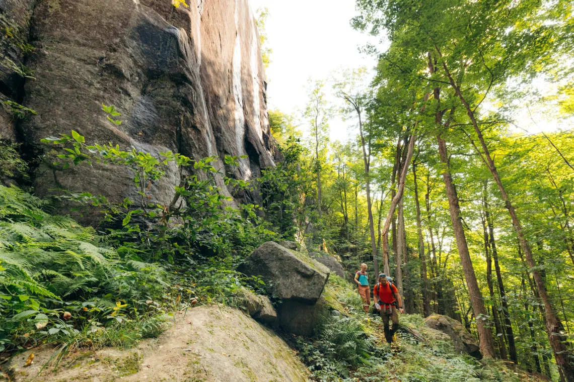 Hikers walk along base of rock face