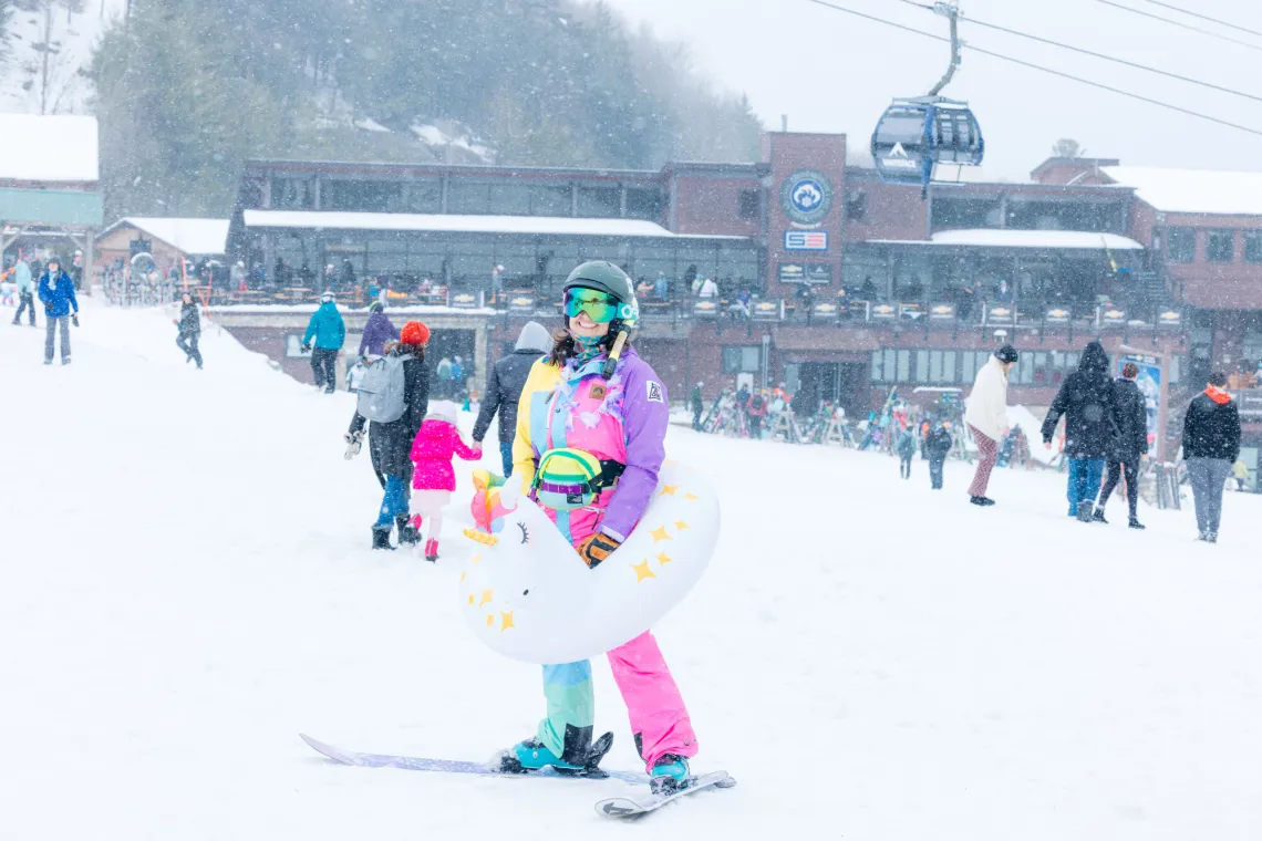 Skier stands in colorful ski gear with unicorn pool floaty around her waist