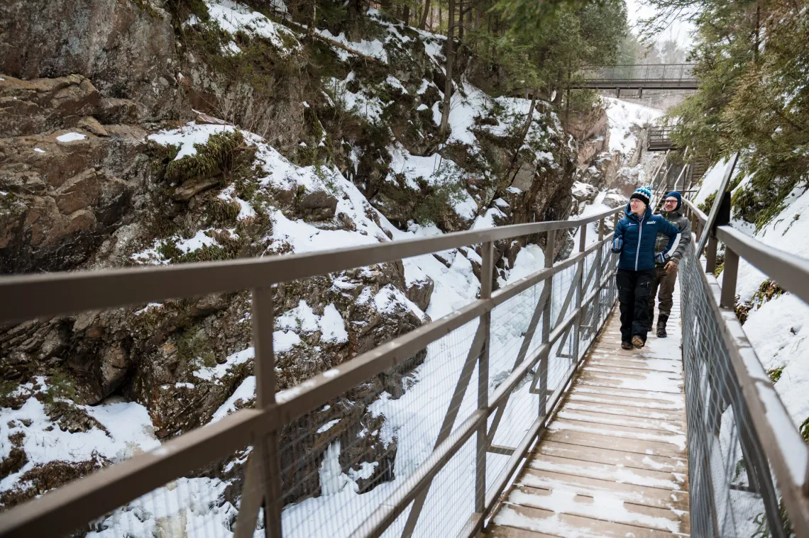 Two people walk on boardwalk over snowy chasm