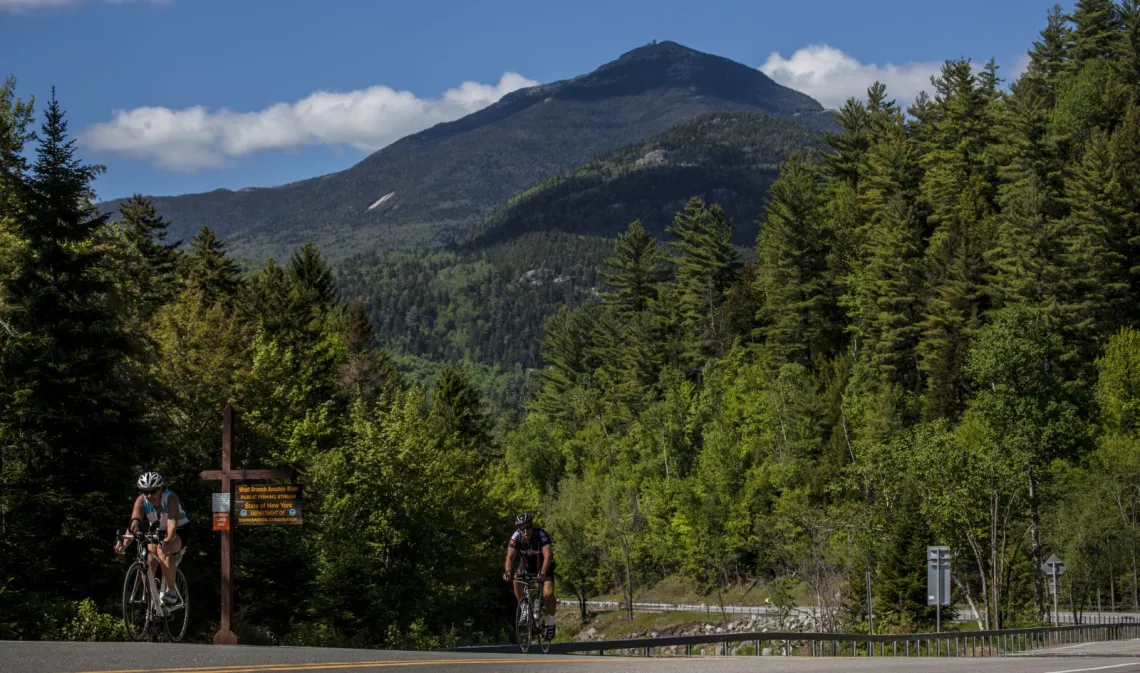 Cyclists ride down a road with a giant mountain in the background.