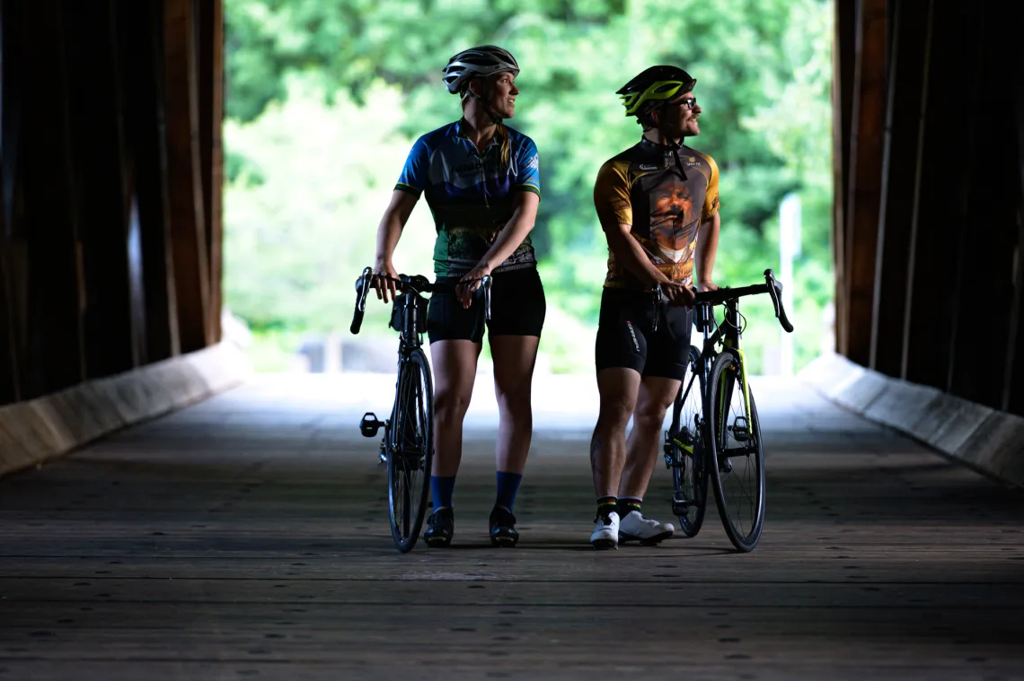 A man and woman walk their bicycles on a covered bridge.