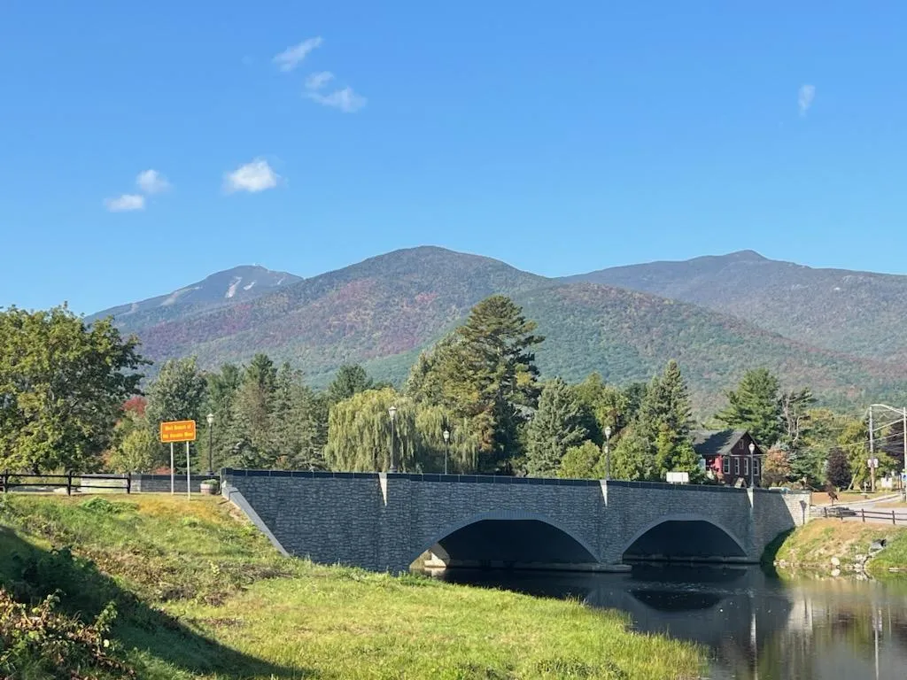 A stone bridge with foliage-covered mountains behind it.