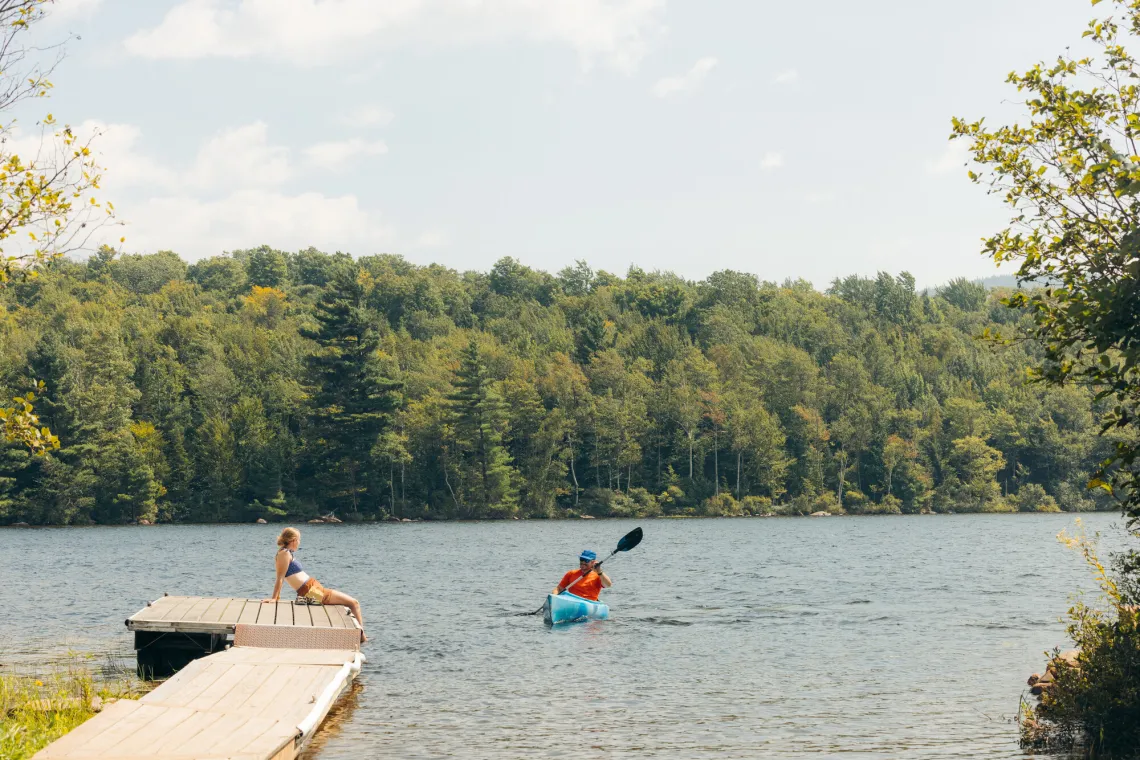 Man in blue kayak paddles towards woman lounging on lakeside dock