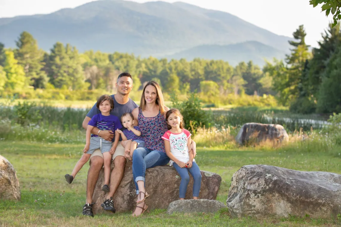 A family sits on the shore of Lake Everest of the Ausable River with mountains in the background.