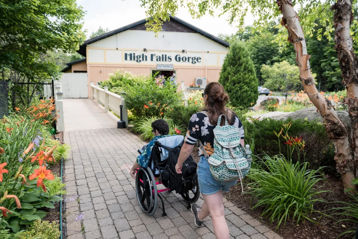 A person follows behind another person in a wheelchair on the walkway towards high falls gorge