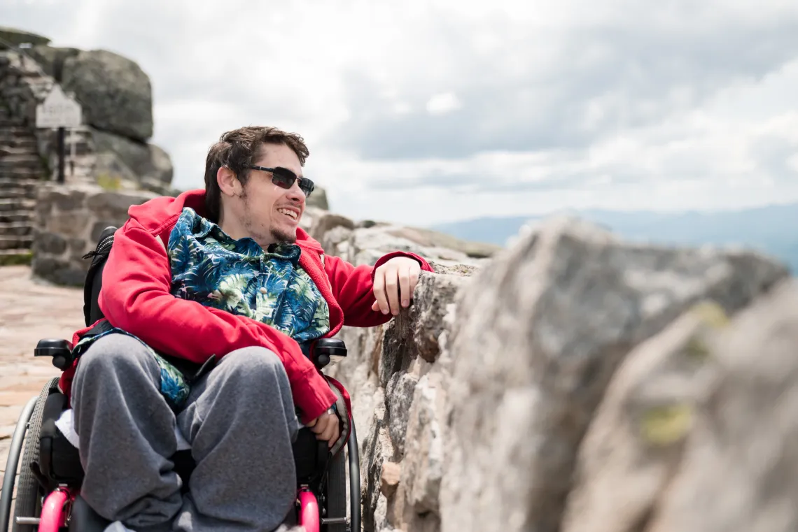 man in a wheelchair looks out at the view of the surrounding high peaks from the parking area of the Whiteface Veterans' Memorial Highway