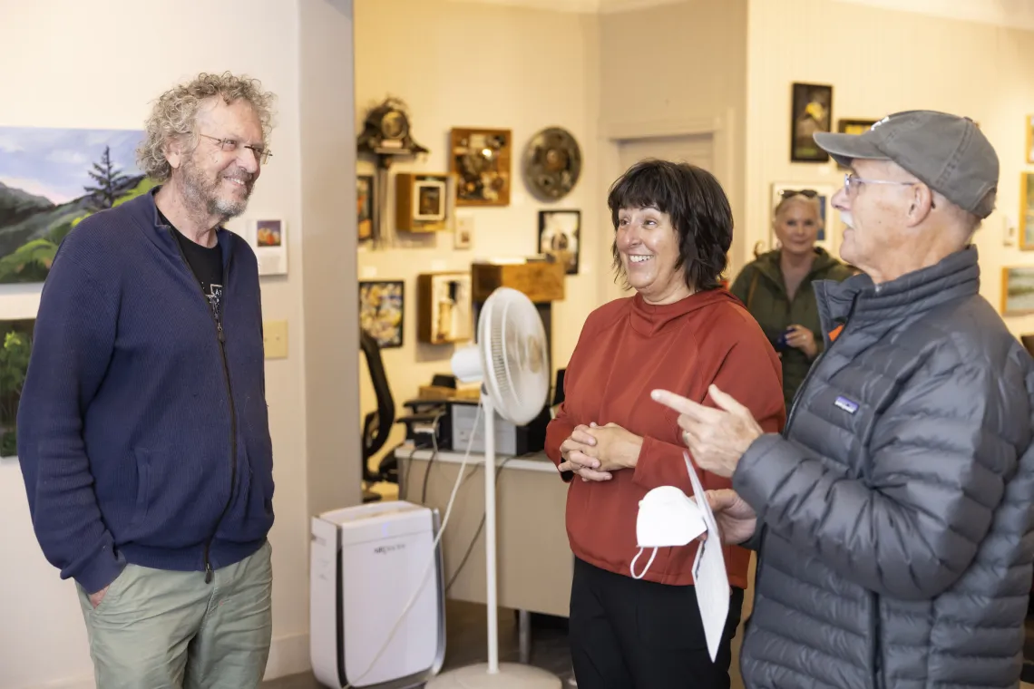 A couple speaks with an artist at a gallery opening.